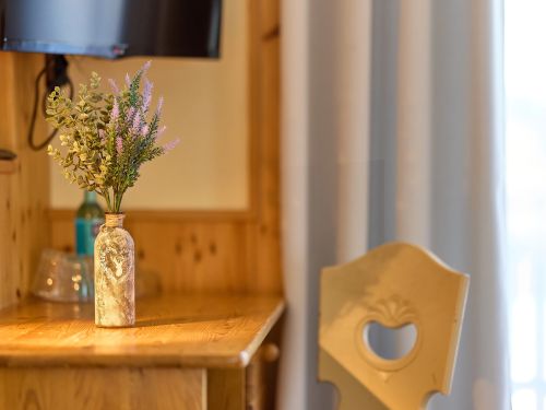 Vase mit Blumen auf einem holztisch eine stuhl und ein fernseher im hintergrund