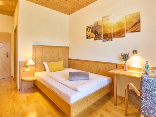 Gemütliches hotelzimmer mit holzbett schreibtisch stuhl und wandbild in warmen gelbtönen und holzboden
