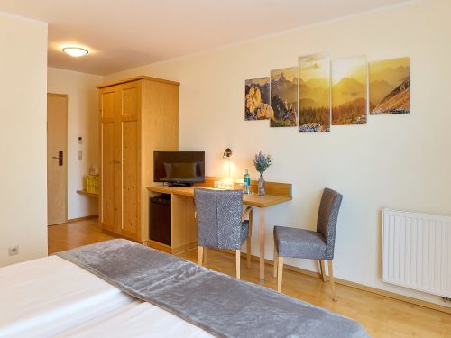Hotelzimmer mit holzschrank tisch stuehle Fernseher und berggemälde an der wand