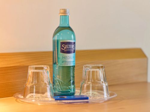 Flasche Mineralwasser zwei umgedrehte Gläser und ein blaues Feuerzeug stehen auf einem Tablett auf einem Holztisch