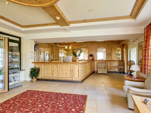 Helle hotellobby mit holztheke ledersesseln pflanzen rotem teppich und karierter gardine am fenster