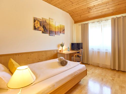 Gemütliches Gästezimmer mit Holzmöbeln Einzelbett Schreibtisch Fernseher und großem Fenster mit Vorhängen