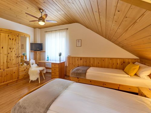 Gemütliches Schlafzimmer mit schrägem Holzdach zwei Betten einem Kleiderschrank und einem Schreibtisch mit Stuhl