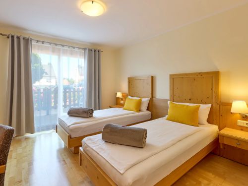 Hotelzimmer mit zwei Einzelbetten Holzmöbel und großer Glasfront mit Gardinen und Balkonblick