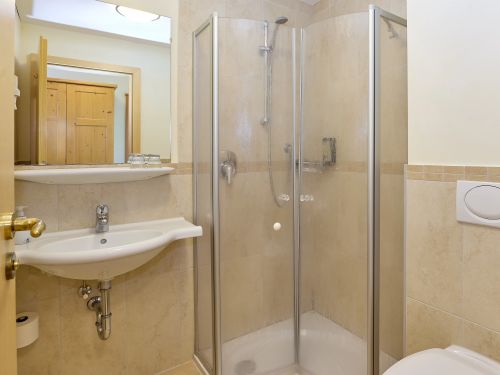 Kleines badezimmer mit dusche waschbecken spiegel und wc in beigen fliesen und holzturen