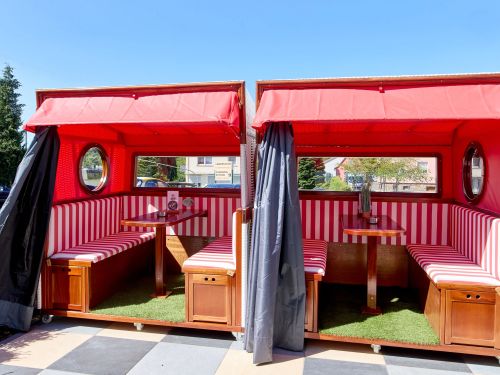 Zwei rote Strandkorb Sitzbereiche mit Tischen gemütlich im Freien bei sonnigem Wetter