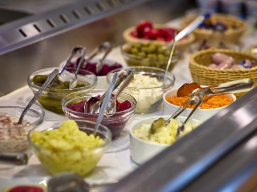 Buffet mit verschiedenen Salaten und Beilagen in Glasschalen und Servierzangen auf weissem Tisch