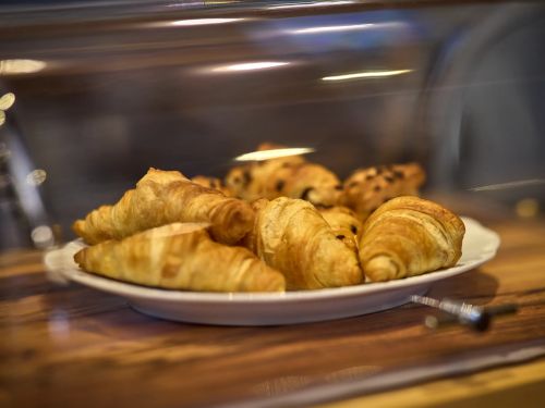 Croissants und süßes Gebäck auf einem Teller hinter einer Glashaube auf einem Holztisch