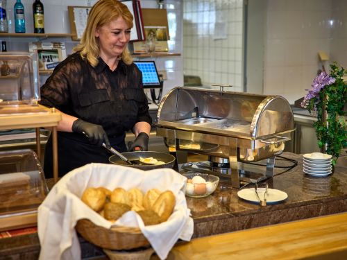 Frau in schwarzem Hemd brät Spiegelei hinter Buffet mit Brötchen und Tischgerät in Restaurantküche