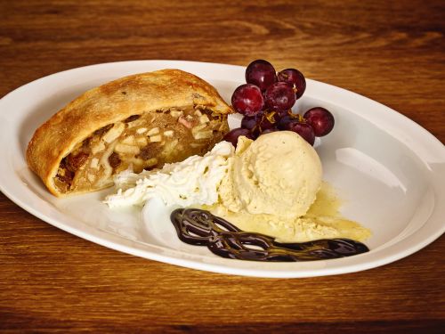 Apfelstrudel mit Vanilleeis Schlagsahne Trauben und Schokoladensauce auf weissem Teller