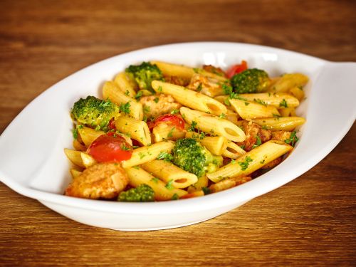 Penne nudeln mit brokkoli kirsch tomaten und gegrilltem huhn serviert in weisser schale auf holzuntergrund