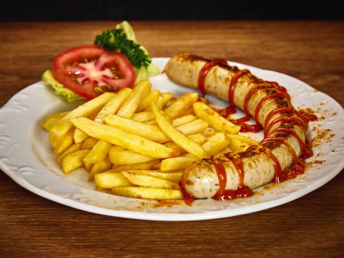 Currywurst mit ketchup pommes frites und tomate auf weißem teller vor holzhintergrund