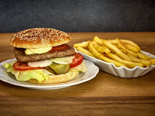 Hamburger mit Salat Tomate Zwiebel Gurke Sauce und Pommes auf Teller vor dunklem Hintergrund