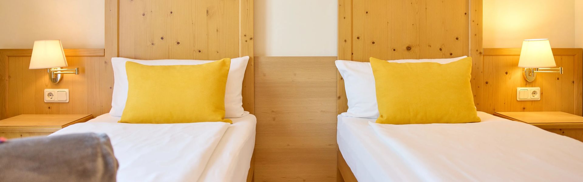 Zwei Einzelbetten mit gelben Kissen Holzkopfteil und Nachttischlampen an hellen Wanden in einem Schlafzimmer