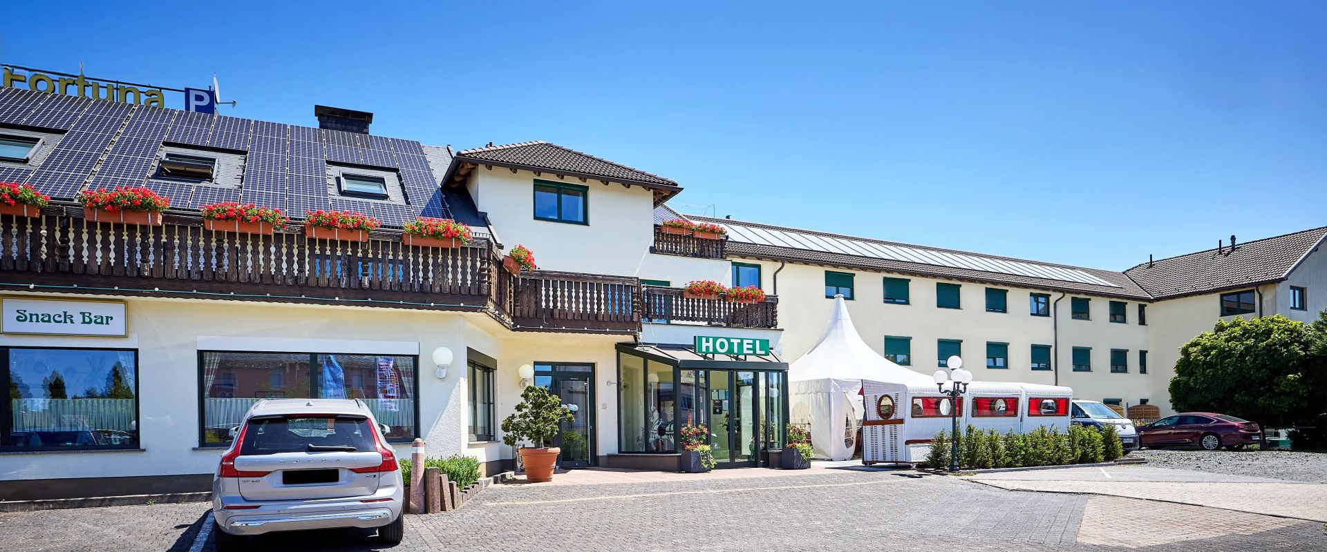 Hotelgebäude mit Balkon und solarzellen vor blauem Himmel parkplatz vor der Eingangstür im sommer